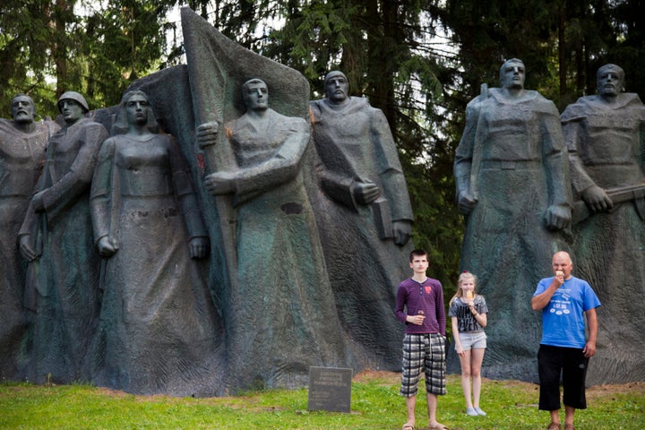 A family awkwardly poses for a photo by a large Soviet soldier statue.