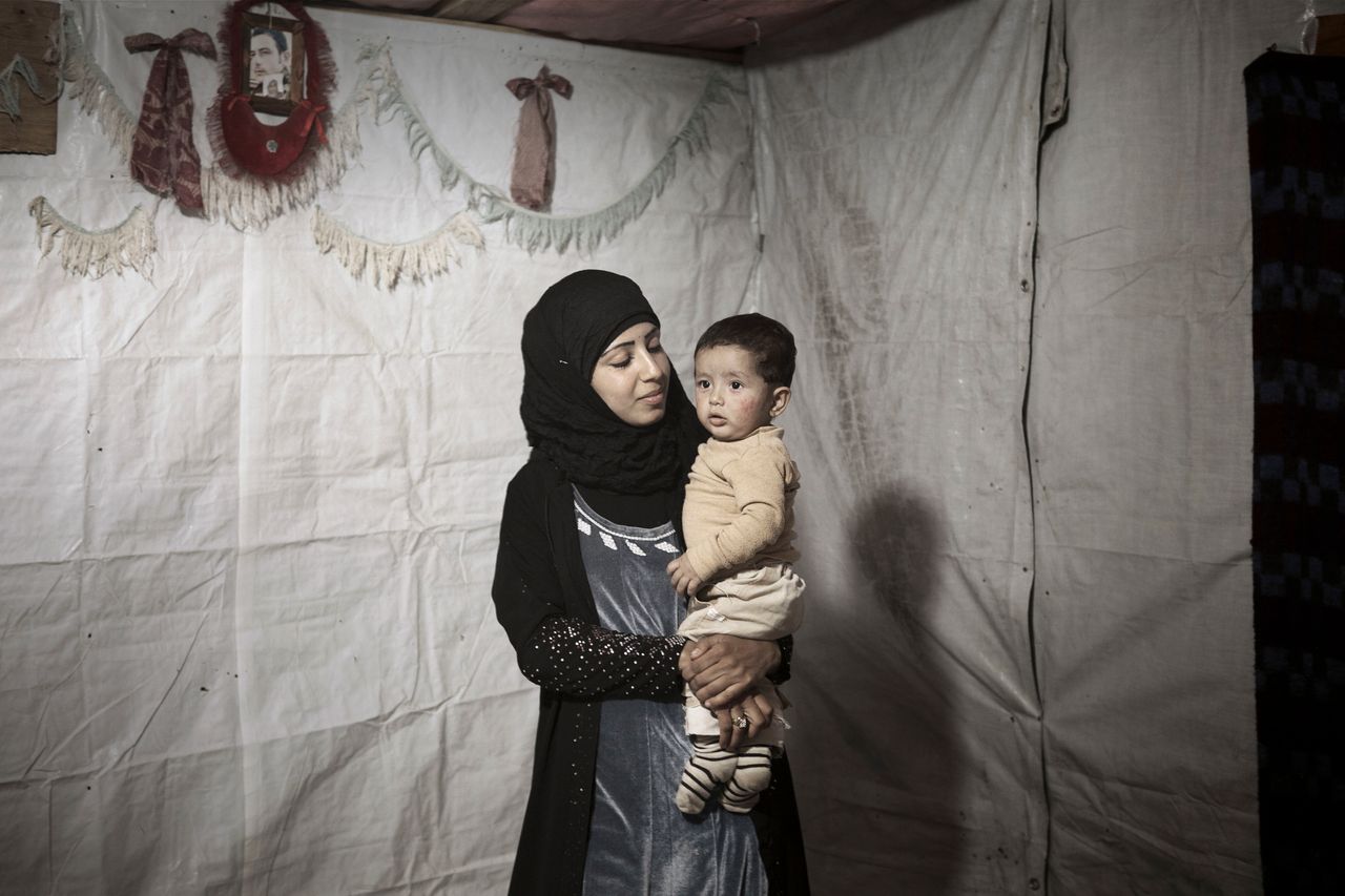 Syrian refugee Amina, 14, holds her young son inside their tent shelter in Bekaa Valley.