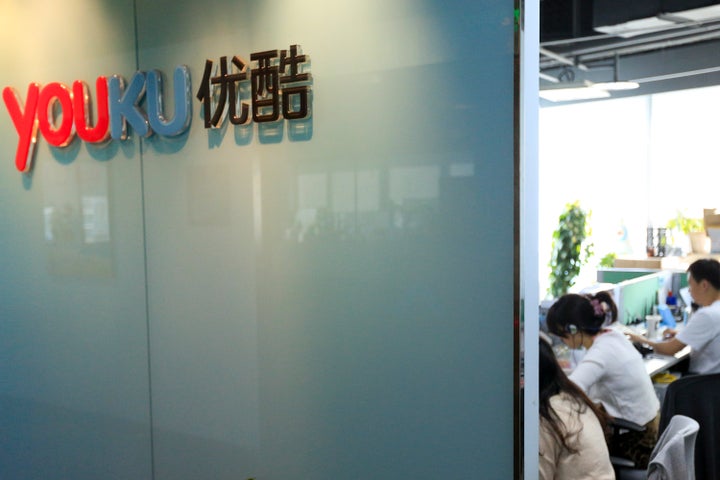 The Youku Tudou Inc. logo is displayed on a wall as employees work at the company's headquarters in Beijing, China. Photograp