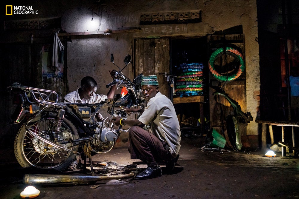 Ibrahim Kalungi and Godfrey Mteza, both 20, work at night in their motorcycle repair shop in Nbeeda, Uganda. The mechanics credit solar lights with enabling them to work longer hours and earn more money.