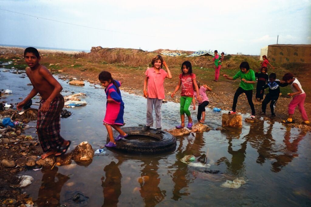 Shot by Nour, age 12,from Homs Governorate, Syria.  Children use rocks and a tire as stepping stones to cross a debris-filled body of water in an informal settlement in the Bekaa Valley, Lebanon, in 2014.
