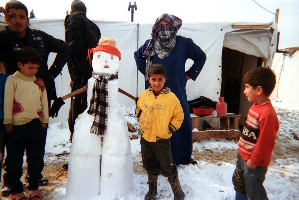 Shot by Akram, age 8, from Aleppo, Syria.<strong><br></strong> Children and adults stand next to a snowman they've made