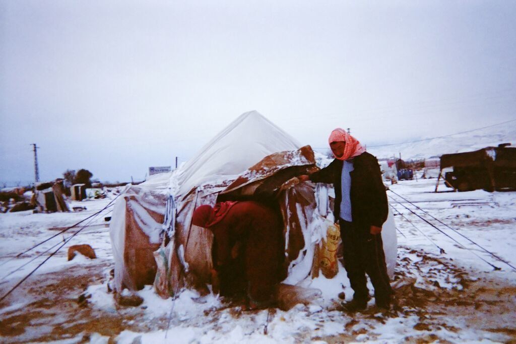 Shot by Ahmad, age 7, from Aleppo Governorate, Syria. A woman and a man remove snow from the entrance to their makeshift shelter in the Bekaa Valley, Lebanon, in 2014.