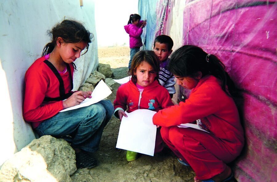 Shot by Ahmad, age 12, from Deir el-Zour, Syria. Children sit on the ground between makeshift shelters to practice reading and writing in the Bekaa Valley, Lebanon, in 2014.