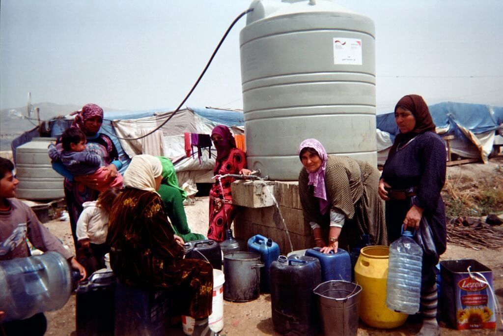 Shot by Riham, age 11, from Homs Governorate, Syria. Women accompanied by children fill jerry cans, pails, plastic bottles and other containers at a water point in an informal settlement in the Bekaa Valley, Lebanon, in 2014.