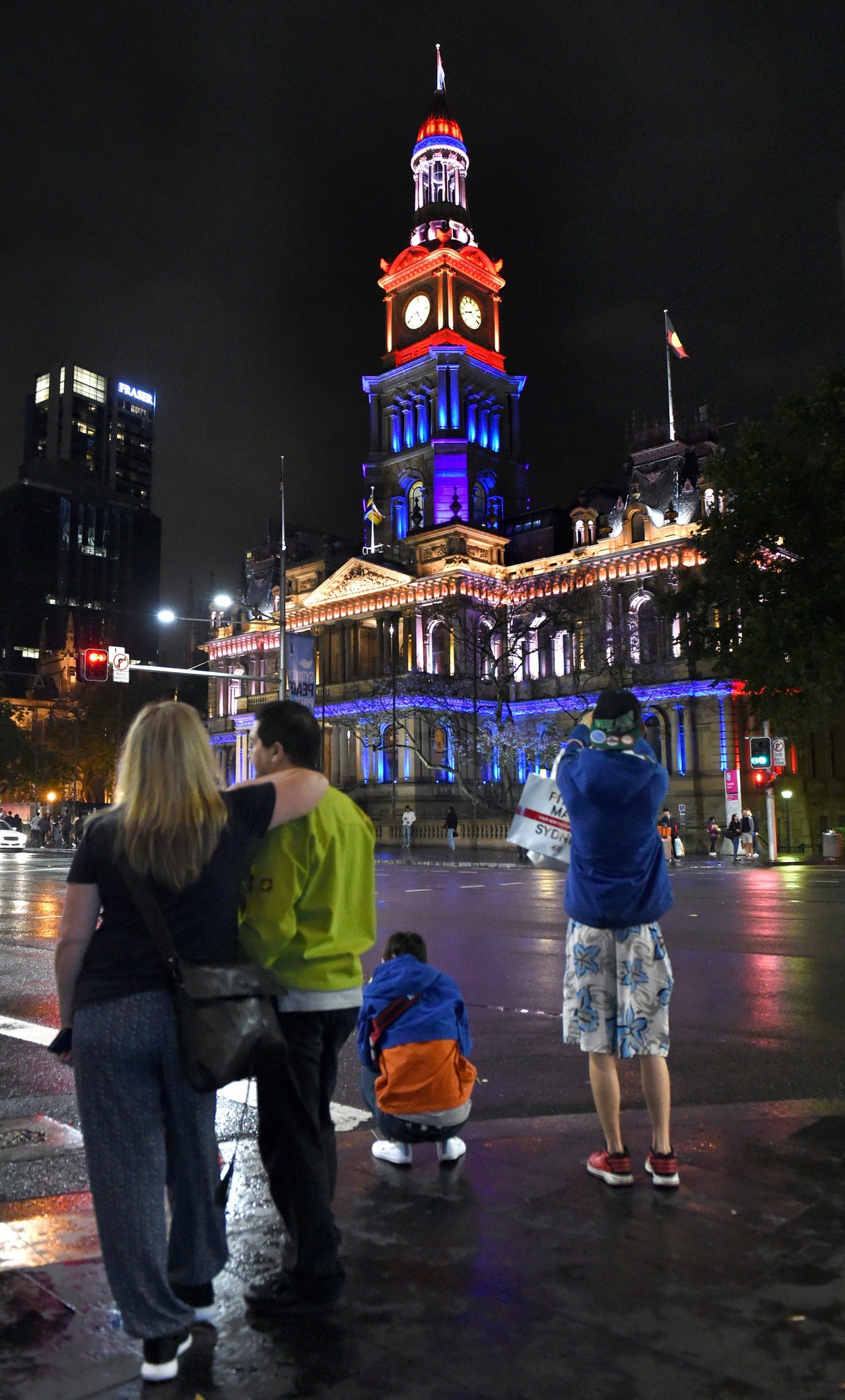 People walk past the Sydney Town Hall as it is lit in the colors of the French flag, on Nov. 14, 2015.