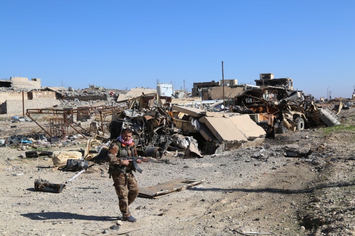 A Peshmerga fighter in front of highly damaged buildings and vehicles after the US-backed Kurdish operation to clear Sinjar o