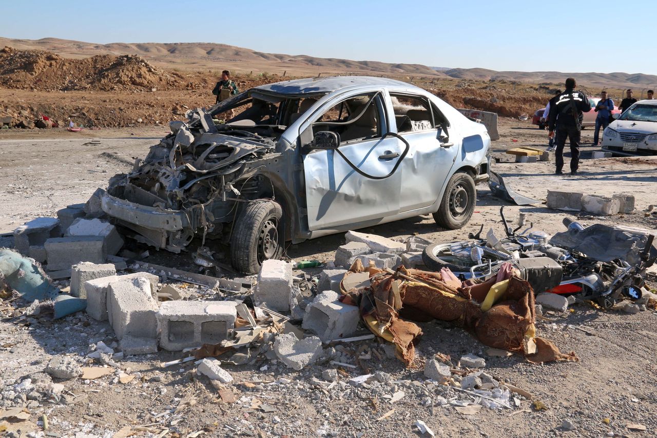 Iraqi men stand next to the wreckage of a car on November 4, 2015, in the aftermath of a suicide bombing by militants of Islamic State jihadist group at a checkpoint at the entrance of the Dibis area, northwest of the Kirkuk provincial capital.