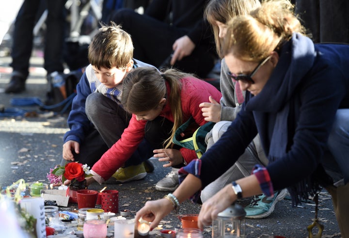 Children and adults lay flowers and light candles at a makeshift memorial along a police cordon set up close to the Bataclan concert hall in Paris.