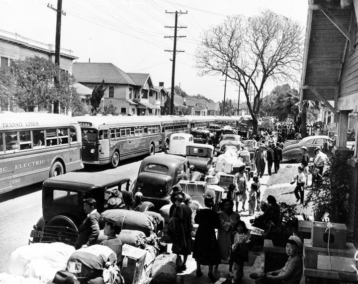 This 1942 photo shows the evacuation of American-born Japanese civilians during World War II, as they leave their homes for internment, in Los Angeles, California. The sidewalks are piled high with indispensable personal possessions, cars and buses are waiting to transport the evacuees to the war relocation camps.