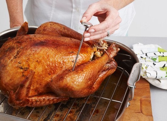 Young woman measuring temperature of whole roasted turkey with meat  thermometer Stock Photo - Alamy