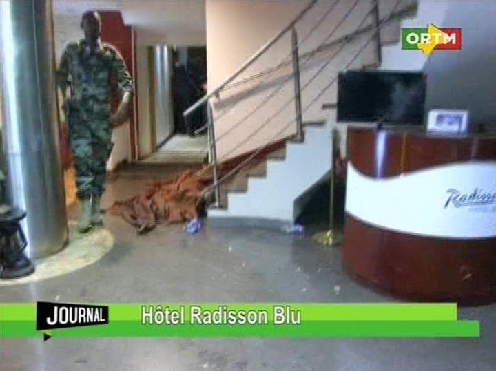 In this TV image taken from Mali TV ORTM, a member of the security forces walks past a body lying covered on the floor in the Radisson Blu Hotel hotel in Bamako, Mali, Friday Nov. 20, 2015.