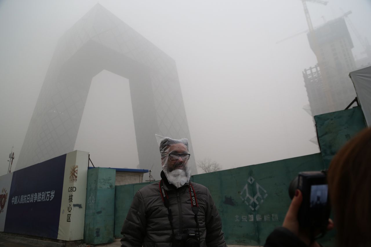 A man wearing a plastic bag stands in front of the CCTV Headquarters in the heavy smog on December 1, 2015 in Beijing, China.