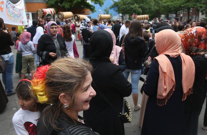 A Bosnian woman, who has dyed part of her hair in the colors of the German flag for the World Cup, and other locals, including Muslim women, watch as a Burundi drumming and dance group affiliated with a local Christian African church perform prior to the arrival of German Interior Minister Thomas de Maiziere in the immigrant-heavy Soldiner Kietz district on June 17, 2014, in Berlin.