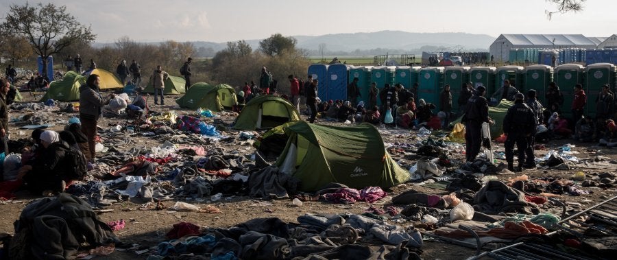 Railway lines cut through the camp, with tents and NGO posts scattered on either side. Discarded blankets, clothes, shoe