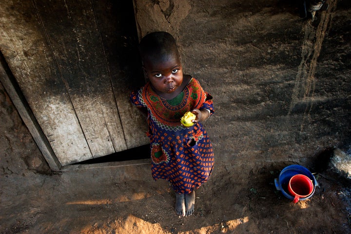 GALUFU, MALAWI - OCTOBER 16: Magreti Nangamtani, age 3, eats a mango outside the family house on October 16, 2005 in Galufu, Malawi. Her mother, Stelia, age 26, and little sister Pilirani, age 2, are one of the poorest families in Galufu, and they have to beg for food every day Magreti has climbed a tree to find a mango to eat as the family doesn't have any maize to cook porridge. Most people in the village are poor and hungry, and cannot afford to buy maize at the market.