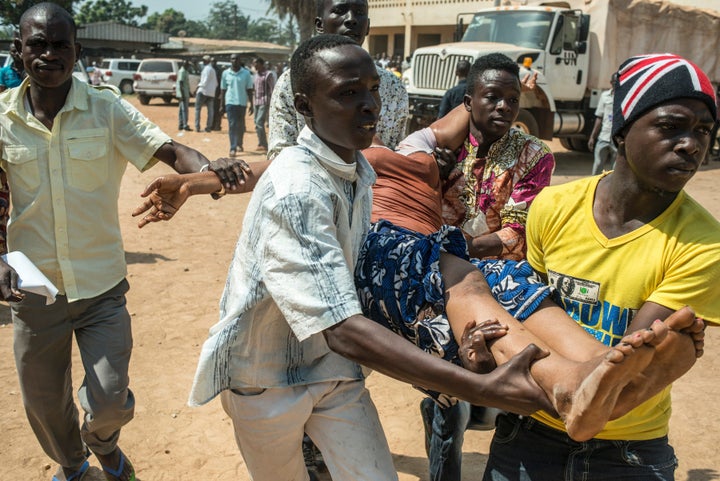 TOPSHOT - A group of men carry a woman who passed out as heavy gunfire is directed towards the Baya Dombia school where voters were gathered for the Constitutional Referendum in Bangui, on December 13, 2015. At least two people died and around 20 were hurt in heavy fighting in Bangui, Central African Republic capital, between supporters and opponents of the constitutional referendum aimed at ending years of bloody sectarian strife and seen as a test run for presidential and parliamentary polls scheduled two weeks later.