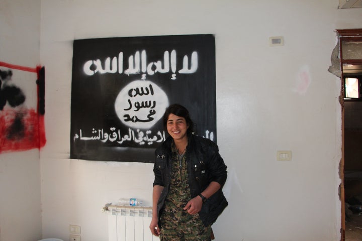 A fighter with the women's arm of the Syrian Kurdish militia, the YPJ, stands before Islamic State propaganda in the town of Tal Hamis, Syria, on February 28, 2015, after Kurdish forces captured it from the extremists.