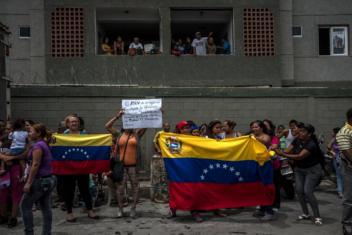 Residents of the Algodonal neighborhood hold national flags and cheer as they watch Venezuelan soldiers take over a warehouse