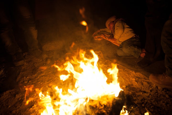 Three young women, the grandmother and five young children warm near a fire. The men are buying food nearby. 