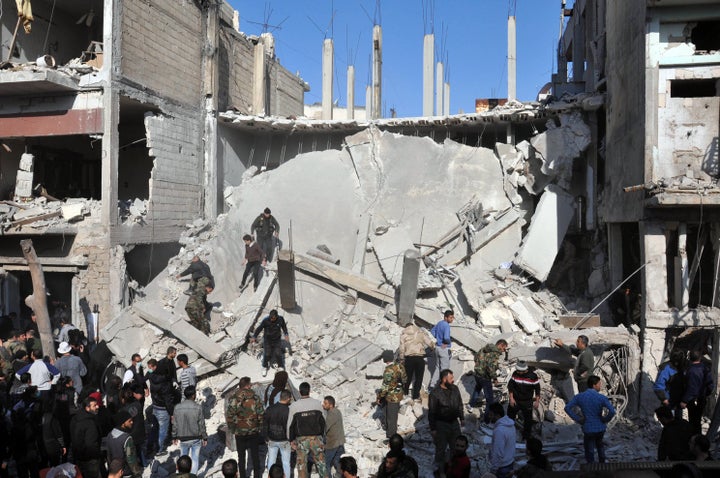 Syrians check the rubble at the site of two car bomb attacks in the al-Zahraa neighborhood of the central Syrian city of Homs
