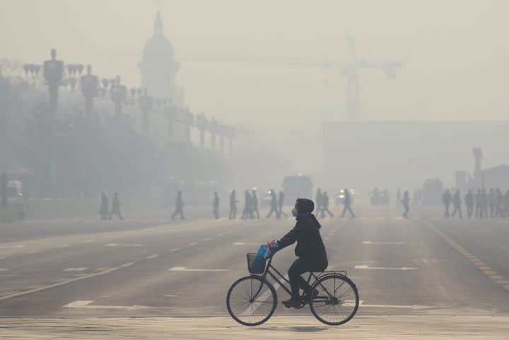 A woman wears a mask as she rides her bicycle near Tiananmen Square on the third day of a 'red alert' for pollution in Beijing on December 21, 2015.