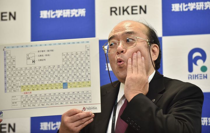 Kosuke Morita, the leader of the RIKEN team, poses with a board displaying the new atomic element 113
