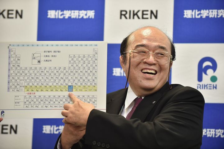 Kosuke Morita, the leader of the RIKEN team, smiles as he points to a board displaying the new atomic element 113.
