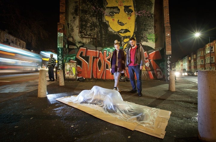 Passersby gaze at a glass sculpture of a homeless person in Bristol, England, crafted by artist Luke Jerram. The goal of the