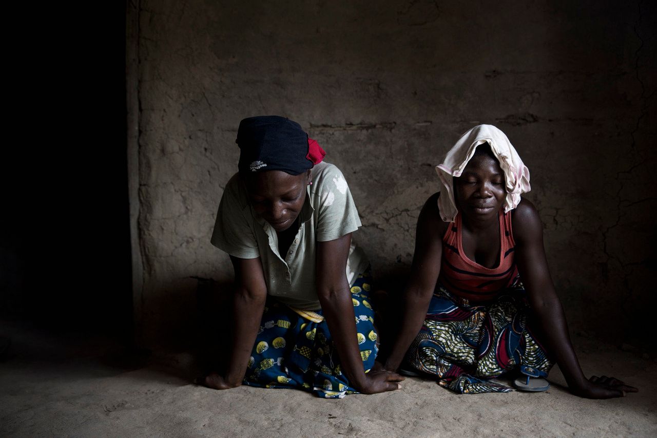 Women pray for the many individuals who never came back from the bush, where they were sent with a bucket of homemade medicine and told to return when they were healed from the virus.