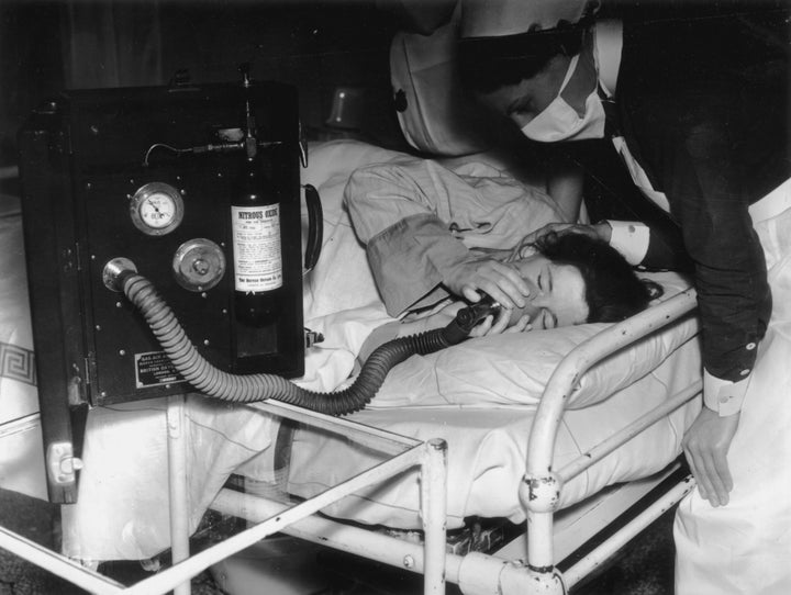 In an effort to make childbirth as painless as possible, a patient inhales analgesia during labor whilst a nurse looks over her in July 1939.