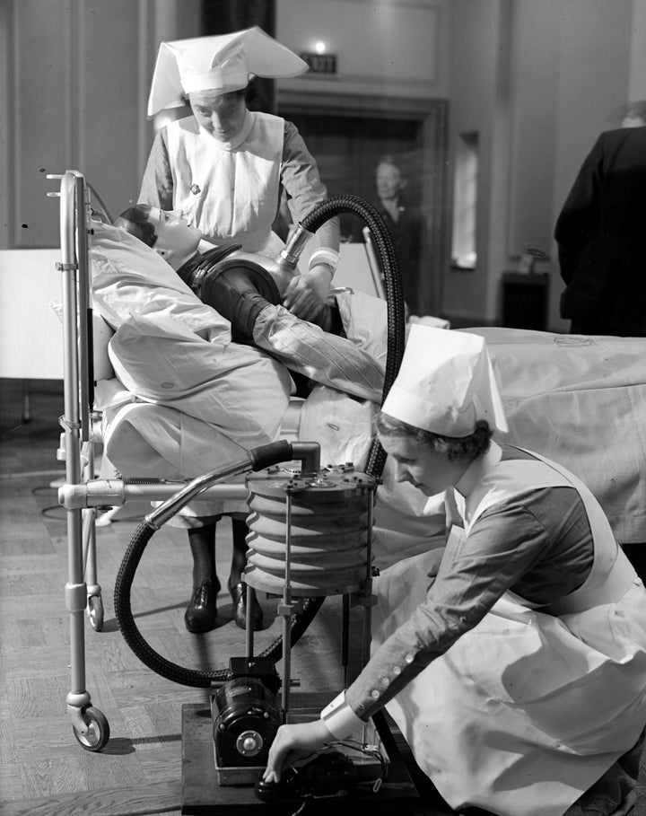 Nurses practice operating a respiratory jacket that performs a similar function to an iron lung, circa 1938.