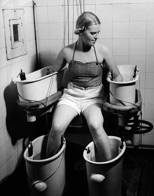 A young woman holds her arms and legs in four water bathes with electric current, to improve blood circulation, circa 1938.