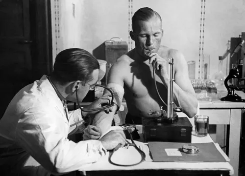 Lieutenant Radtke presses air into his lungs in a constant height with a mercury column, while the doctor checks his blood presssure, circa 1932.