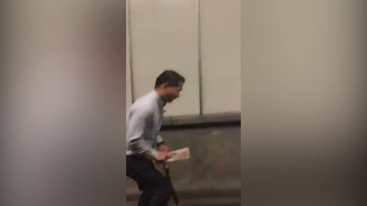The man is seen wearing a white collared shirt and pants and carrying something in his hand.