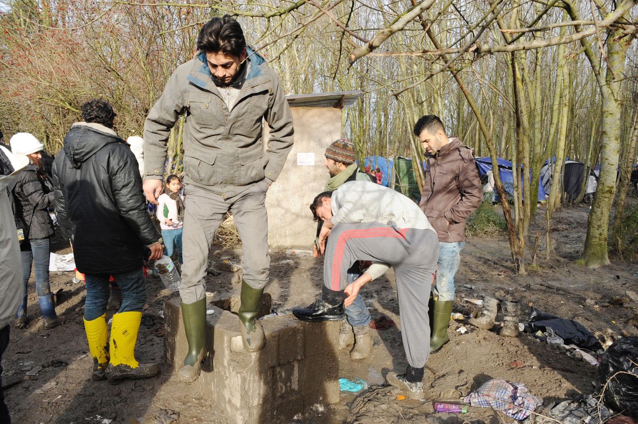 Men gather around the camp's only spigot to wash the mud off of their shoes.