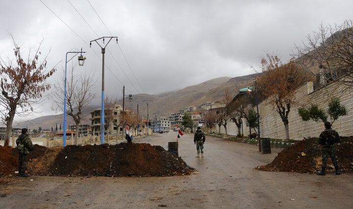 Syrian pro-government forces stand at the entrance of the besieged rebel-held town of Madaya as they wait for a convoy of aid from the Syrian Arab Red Crescent on Jan. 14, 2016.