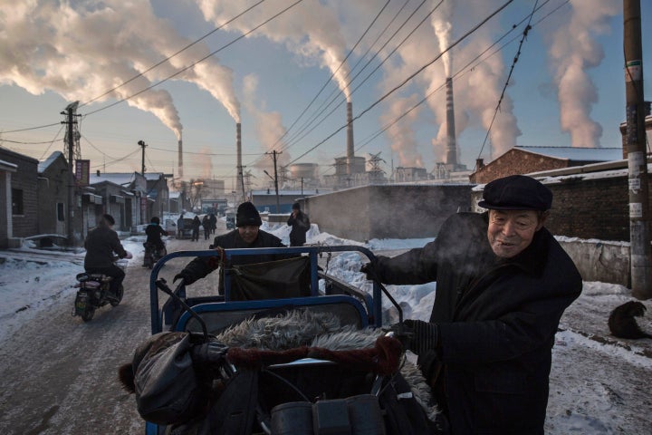 Smoke billows from stacks as Chinese men pull a tricycle in a neighborhood next to a coal fired power plant on November 26, 2