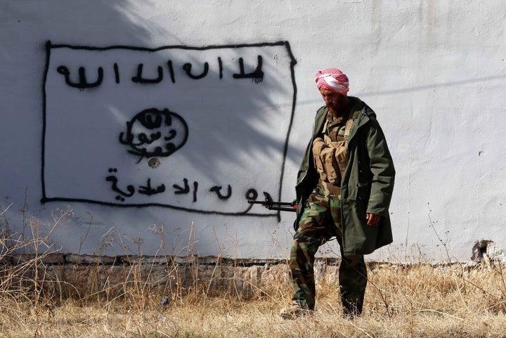 A fighter walks by a wall bearing a drawing of the self-described Islamic State's flag in Sinjar, Iraq. The United Nations said Tuesday that the Islamic State group are holding about 3,500 people as slaves.