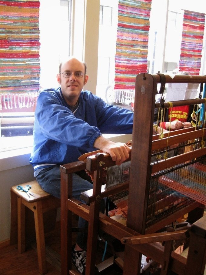 A man looks up from a loom at Flying Shuttles Studio, a Rhode Island nonprofit that supports artists and weavers with intellectual and developmental disabilities. Flying Shuttles rugs are sold at Inner Space.