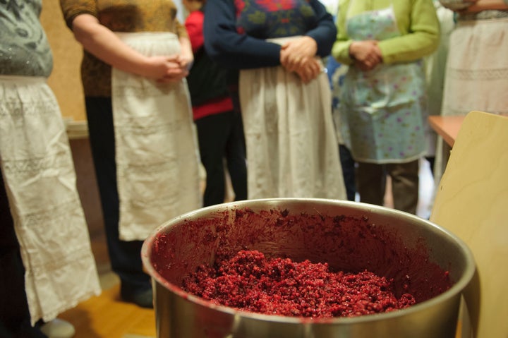 Women stand behind a pot filled with grain porridge during the preparation of Estonian blood sausages.