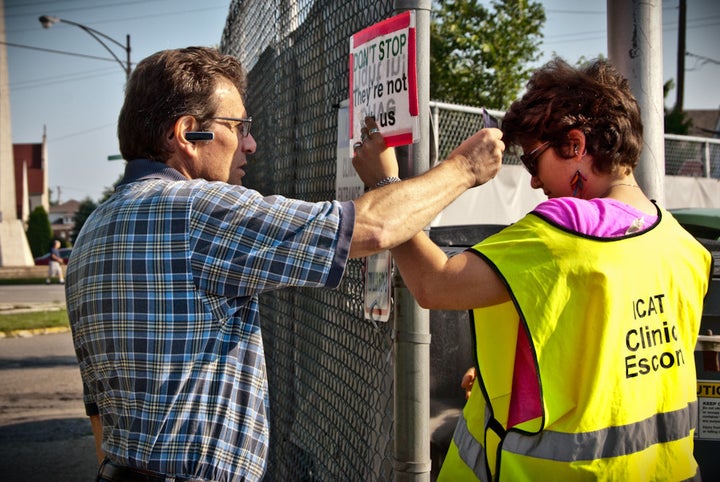 A clinic escort and a protester face off. She looks down to check his feet are not over the property line while he yells at h