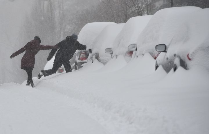 People cross a snow bank to get to the sidewalk on a residential street in Washington, DC on Saturday.