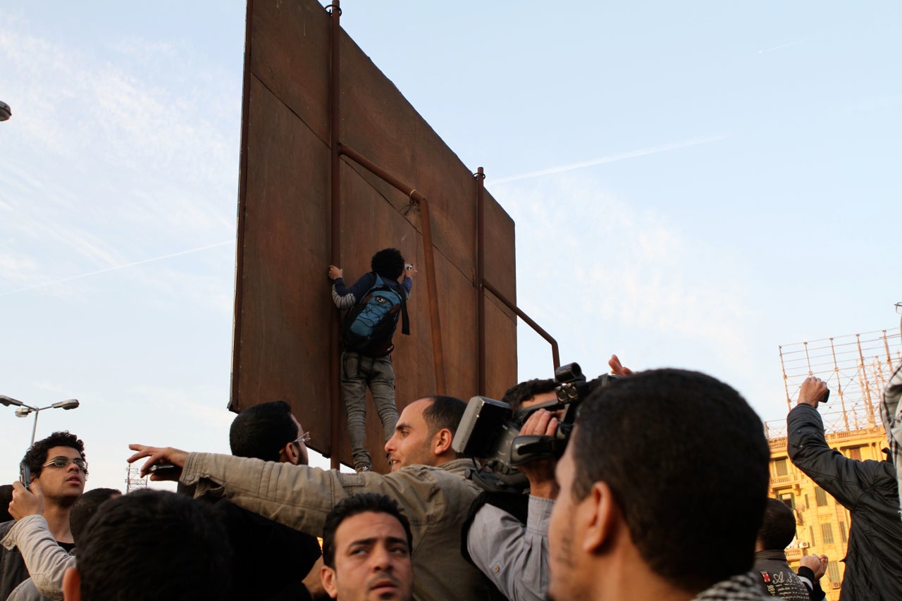 Ganzeer's art played a public role during the 2011 protests in Tahrir Square. Here the artist can be seen at work above the crowd.