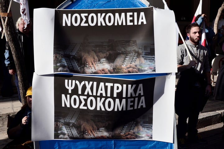 A protester stands by banners reading "hospitals" and "mental hospitals" during a demonstration by health workers and hospita