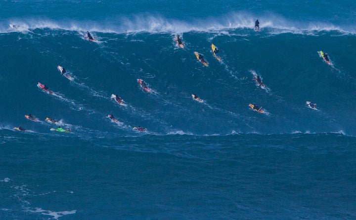 At Waimea Bay, surfers try to paddle over the crest before the powerful wave curls over itself.