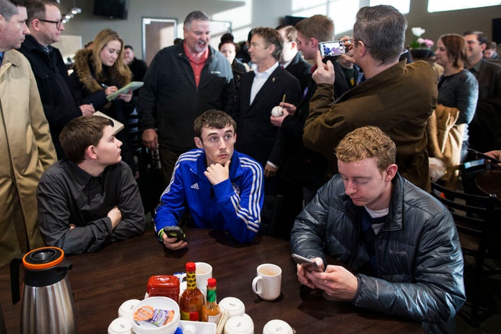 A man looks up from his phone as Republican presidential candidate Sen. Rand Paul (R-Ky.) greets supporters behind him at a campaign stop with Sen. Charles Grassley (R-Iowa) at the Hy-Vee grocery store in Waukee, Iowa, on Monday.