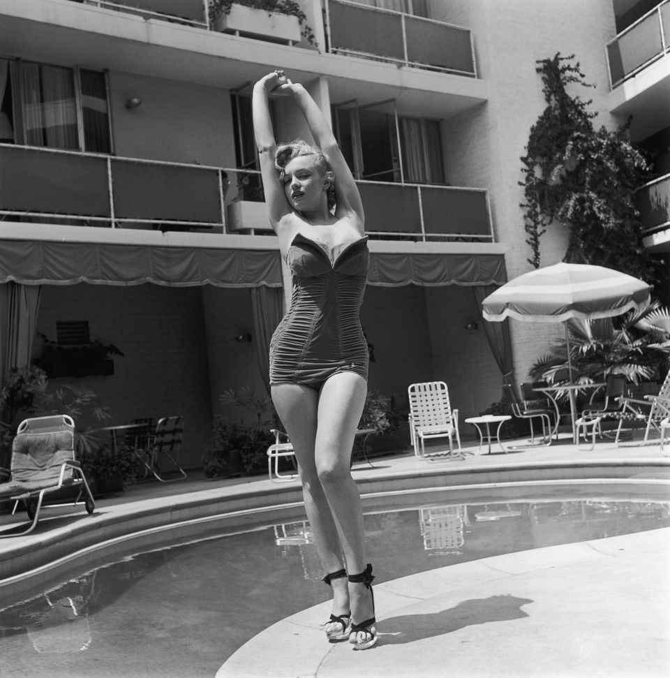 Marilyn Monroe stands next to a swimming pool in a strapless swimsuit and h...