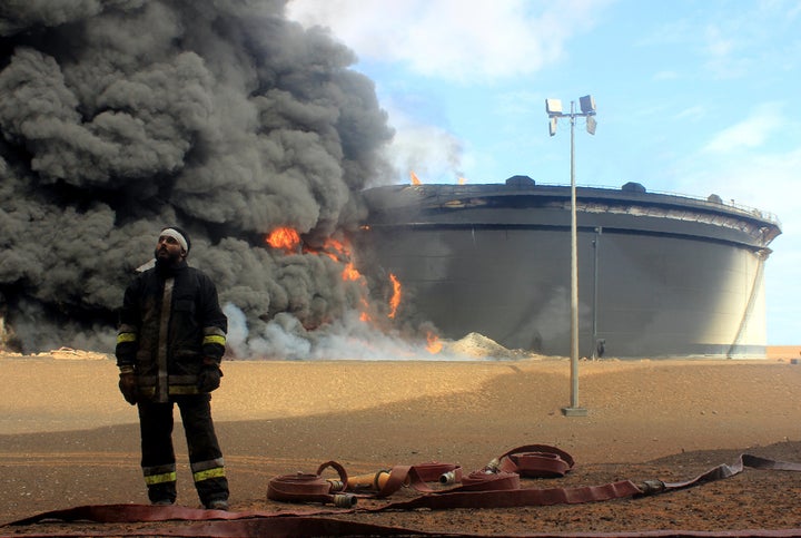 A Libyan firefighter stands in front of smoke billowing from an oil storage tank that was attacked by ISIS militants in Ras Lanouf, Libya.