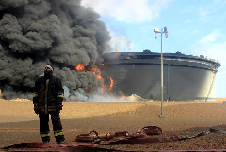 A Libyan firefighter stands in front of smoke billowing from an oil storage tank that was attacked by ISIS militants in Ras Lanouf, Libya. 